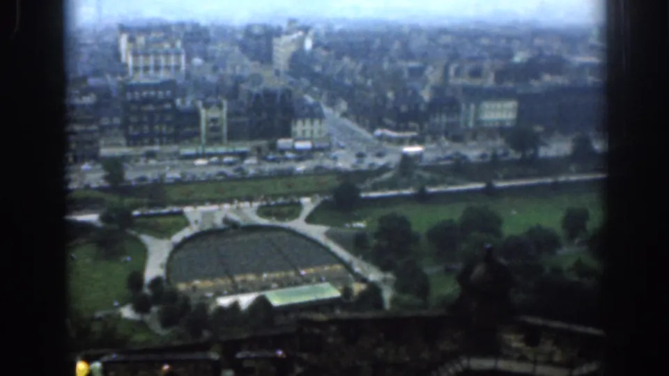 Elevated 1961 London cityscape showing traffic, masonry buildings, trees, lawns, and a circular park structure under haze.