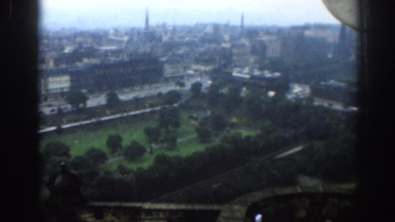 Soft 8mm view over 1961 London, showing parkland, street traffic, urban buildings, distant spires, and dark frame edges.