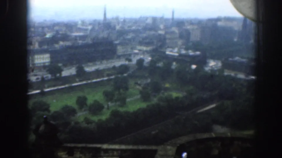 Soft 8mm view over 1961 London, showing parkland, street traffic, urban buildings, distant spires, and dark frame edges.