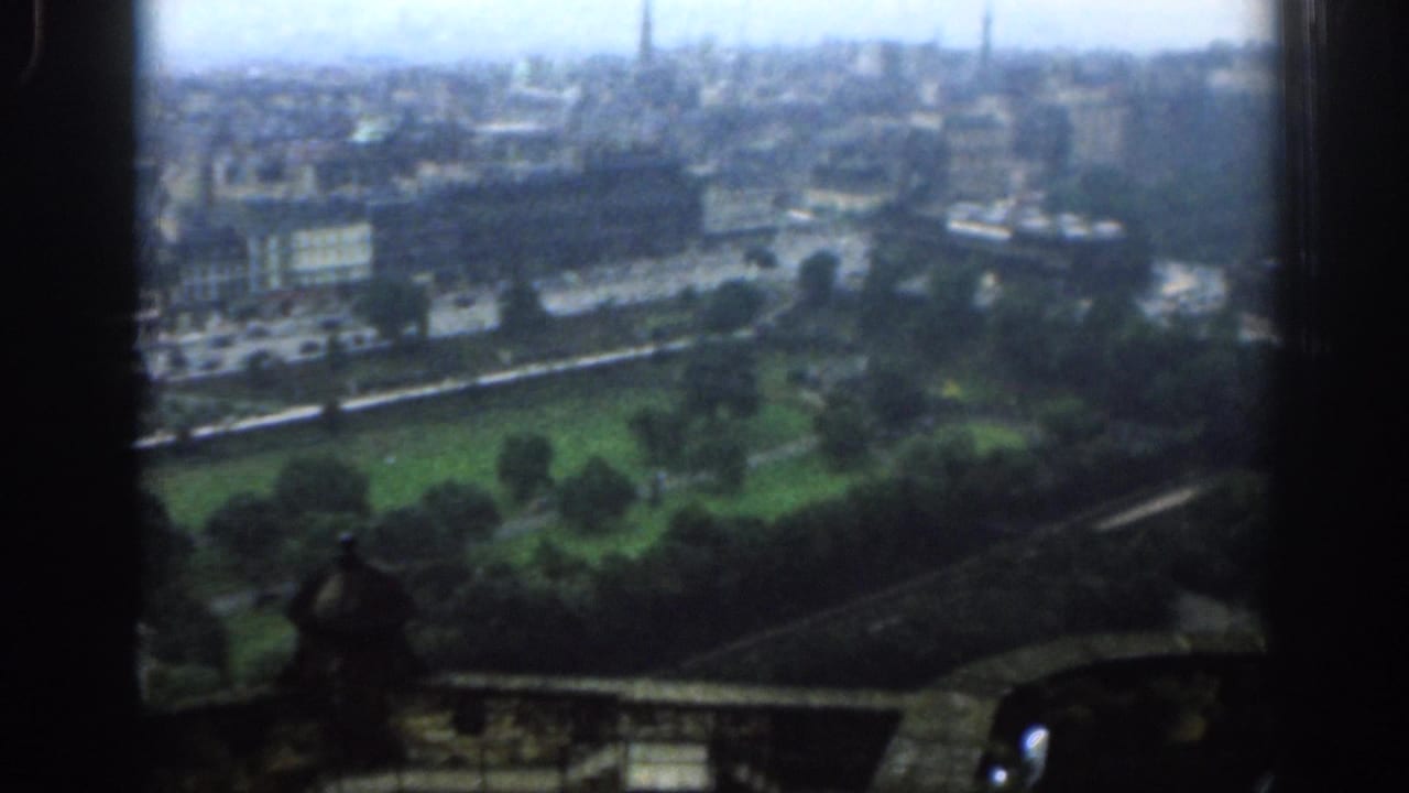 Elevated view over a green park and London city buildings through a dark window edge.