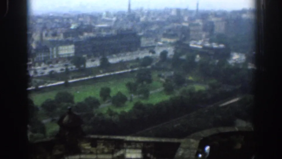1961 London home-movie frame showing a high view across a large park, roads, rooftops, and distant steeples through a dark frame edge.