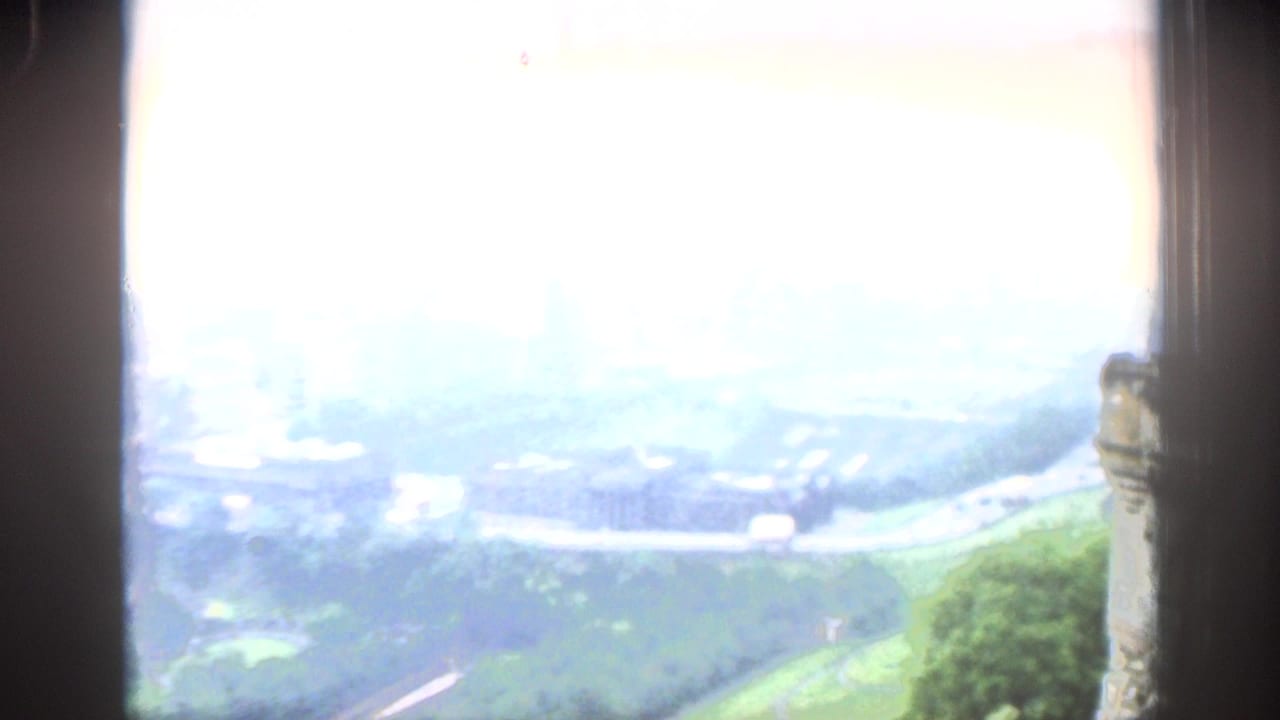 Overexposed high view of parkland, roads, and distant city forms from a window.