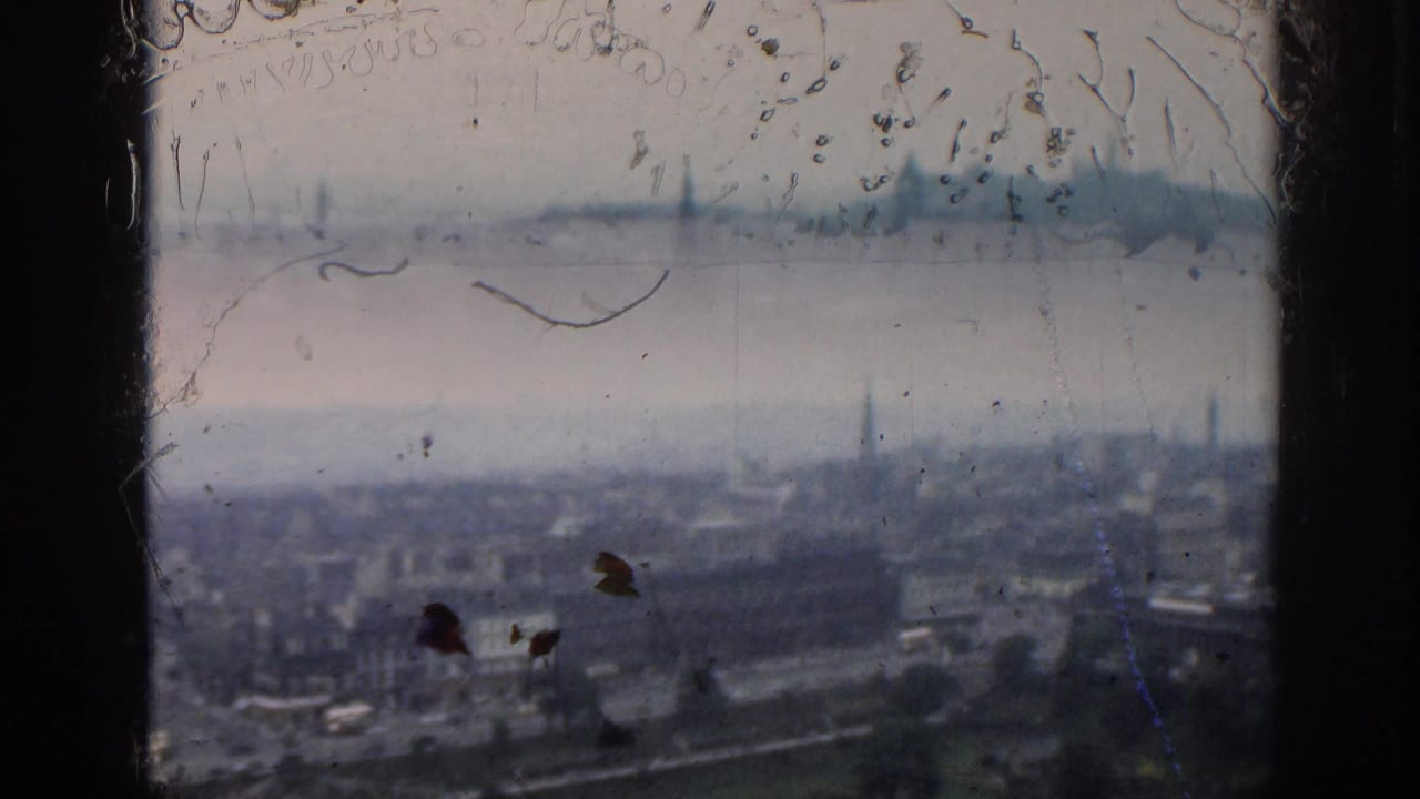Dust- and scratch-marked 1961 London frame with rooftops, roads, a park edge, and distant steeples seen from a high vantage point.