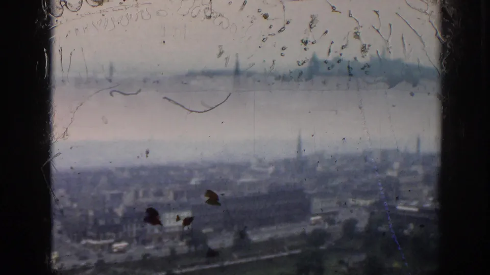 Dust- and scratch-marked 1961 London frame with rooftops, roads, a park edge, and distant steeples seen from a high vantage point.