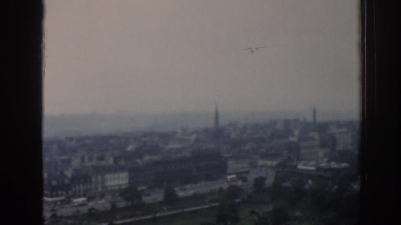 Hazy city skyline seen through dark vertical window or film-frame edges.