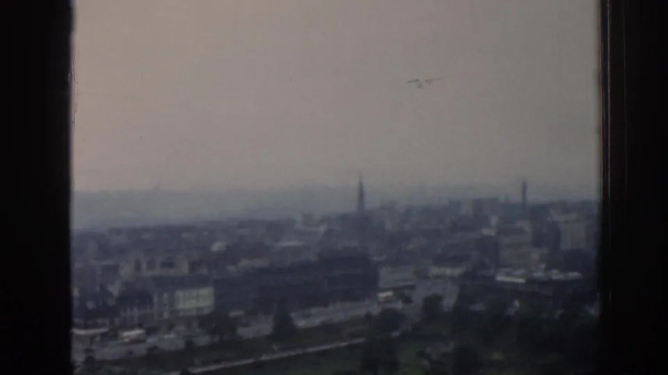 1961 London skyline appears hazy and distant, framed by dark vertical edges in soft 8mm home-movie footage.
