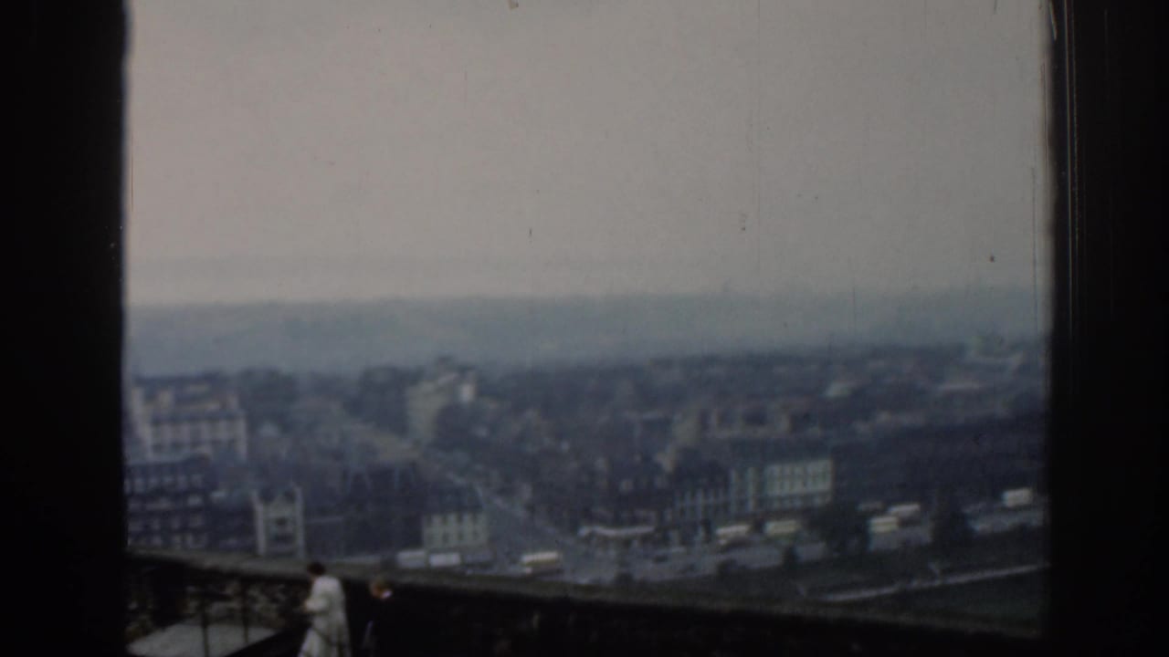 Elevated 1961 London city view with distant streets and buildings, plus small visitor figures near a foreground railing.