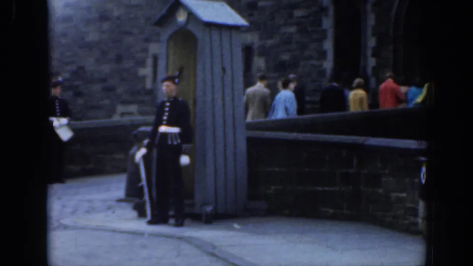 A uniformed guard in London stands beside a small sentry box as pedestrians pass along a stone-walled public viewpoint.