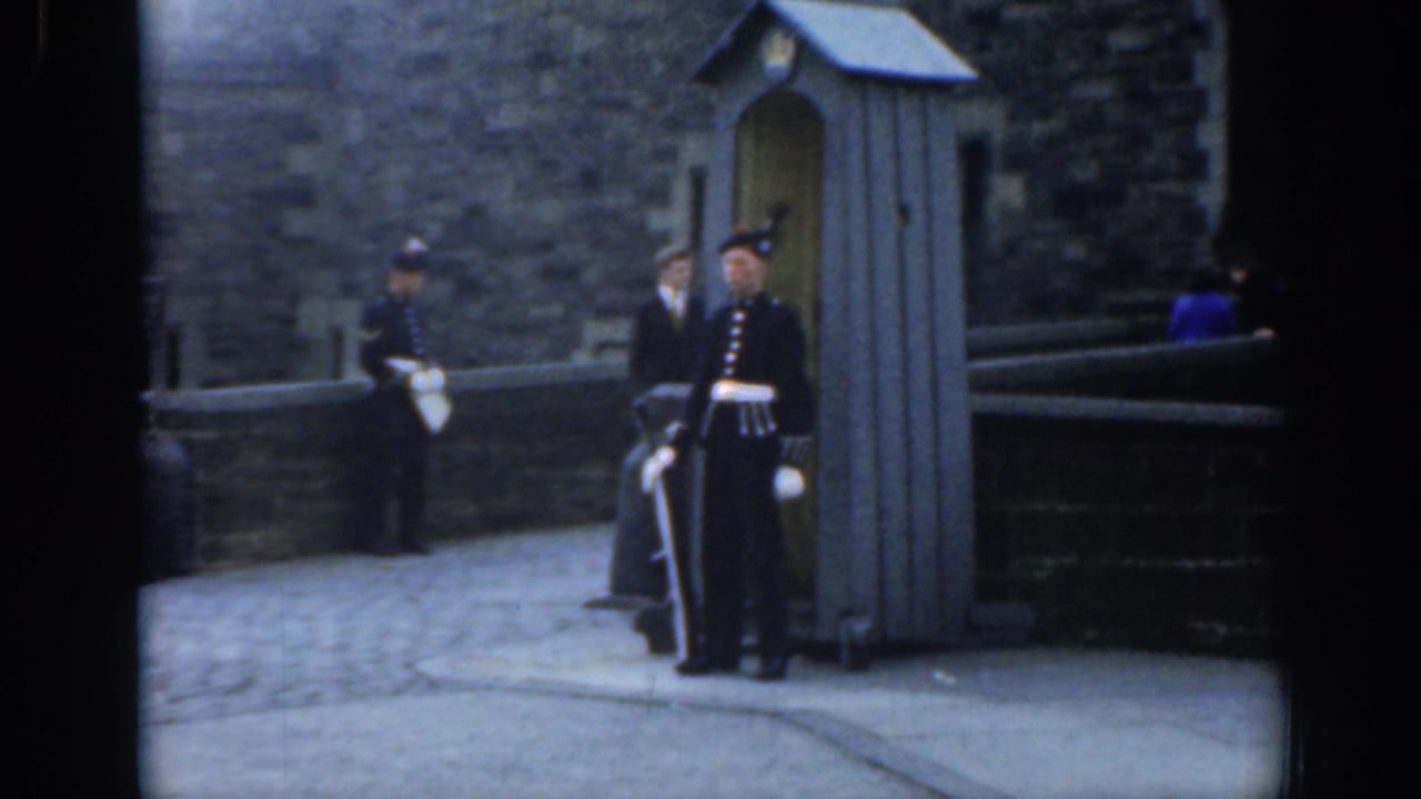 Soft 8mm frame from 1961 London showing guards at attention near a wooden sentry box and stone entrance area, with visitors partly visible.