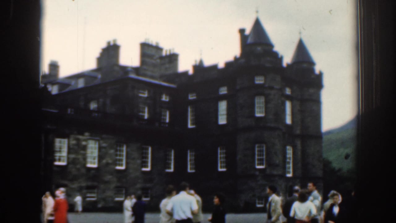 1961 travel frame showing a large dark historic building with turrets, chimneys, windows, and tourists gathered in the foreground.