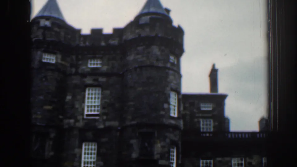 1961 London home-movie frame with a closer handheld view of round turrets, sash windows, and adjoining stonework.