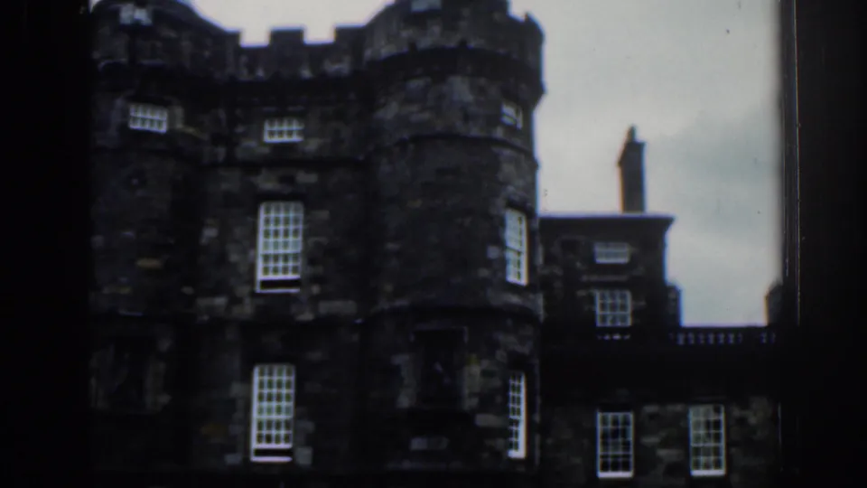 1961 London frame showing dark stone castle-like architecture, including a round turret, windows, and connecting facade.