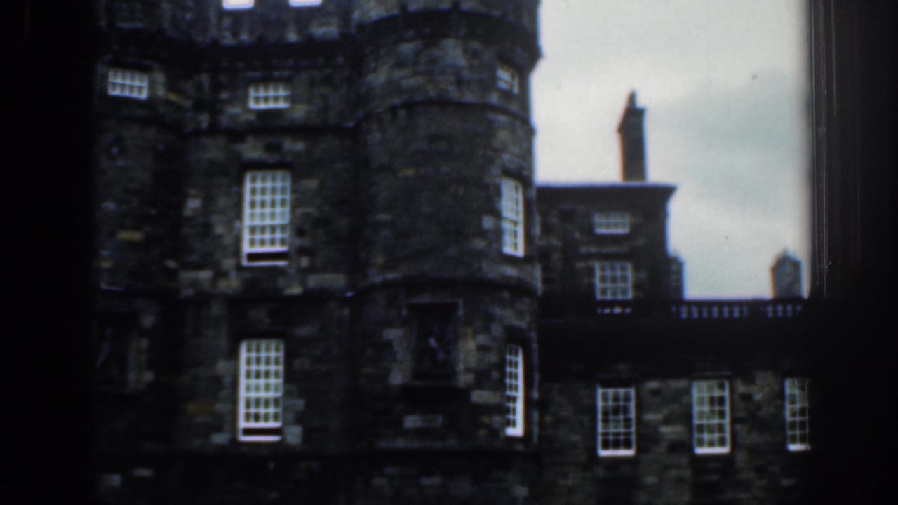 1961 8mm view listed as London, showing a historic dark stone building with rounded towers and white-paned windows through a window frame.
