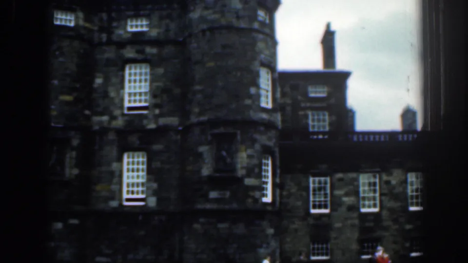 Historic stone building listed as London, with rounded tower sections, white-paned windows, chimneys, and a dark vertical frame edge.