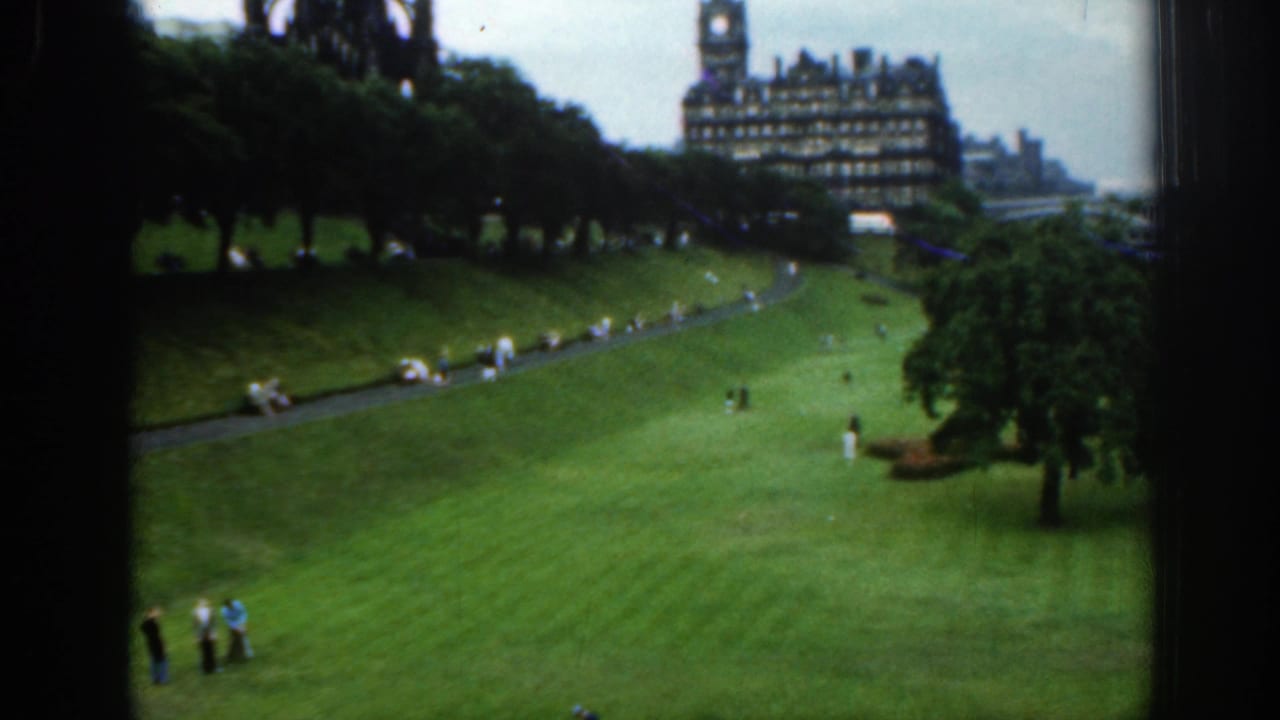 1961 London home-movie view across a landscaped lawn and footpath, with visitors in the foreground and an ornate building beyond trees.