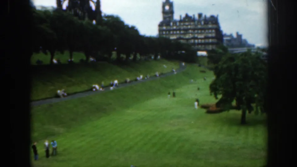 1961 Scotland home-movie frame showing a green park, scattered visitors, trees, and a castle-like building beyond the lawn.