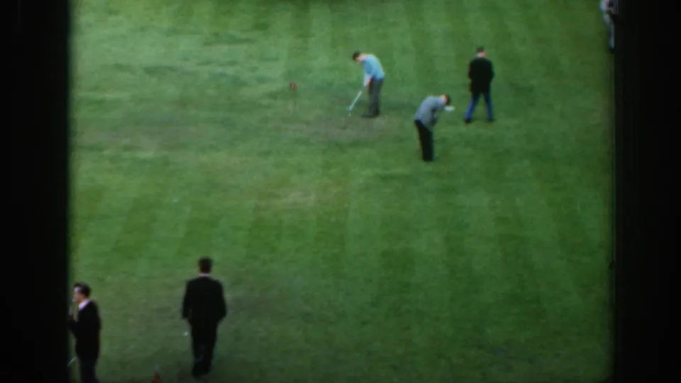 1961 Scotland home-movie frame with men practicing golf on an open green, seen from a raised stationary angle.
