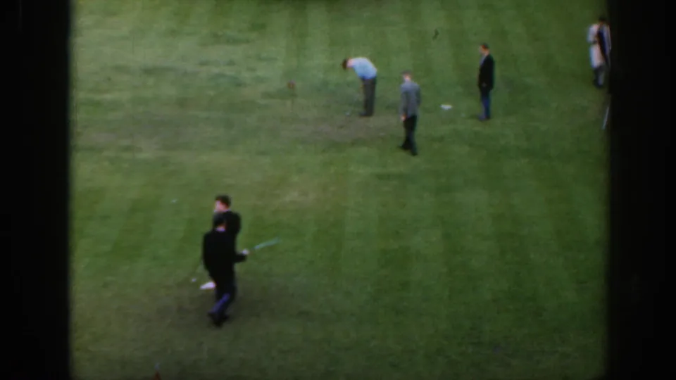 1961 Scotland home-movie frame with golfers spaced across a lawn, including one man walking with a club in the foreground.