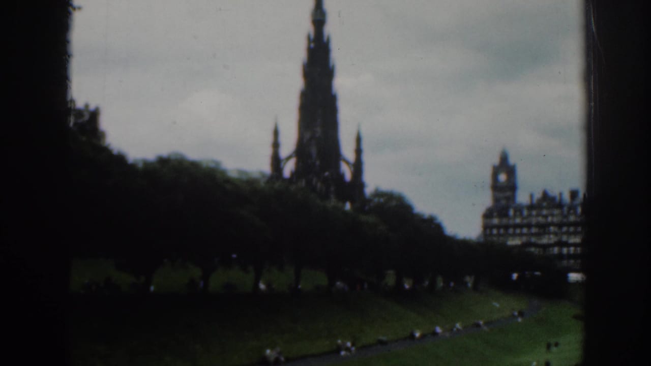Dark window-framed view of the Scott Monument above green parkland.
