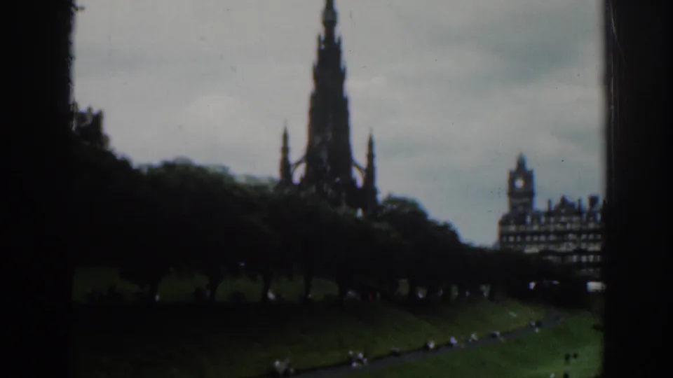 1961 Scotland 8mm frame showing the Scott Monument in Edinburgh beyond trees and grass, partly obscured by dark window edges.