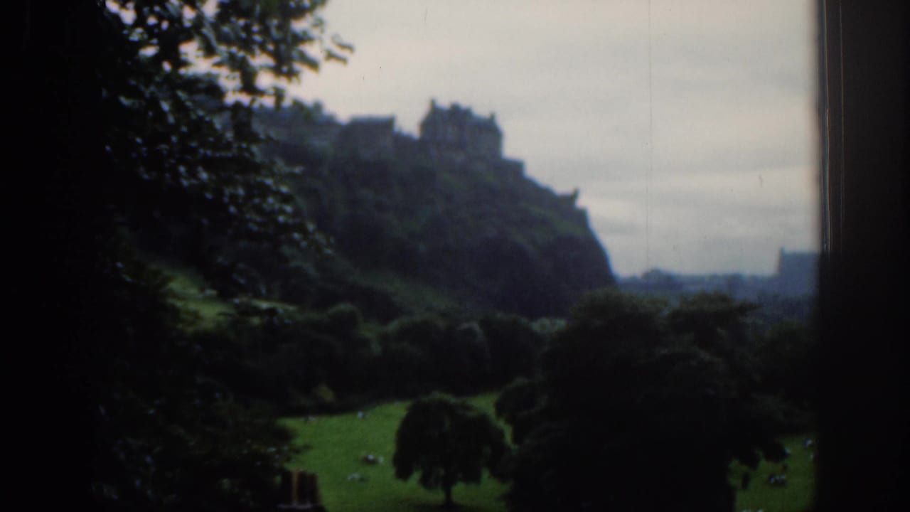 Edinburgh Castle on a wooded hill above dark foreground trees and grass.