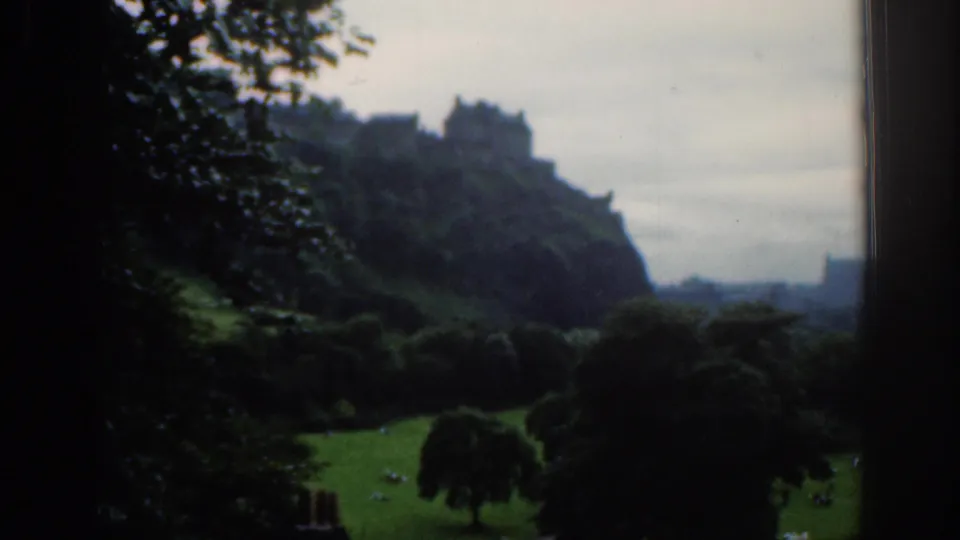 1961 Scotland 8mm frame of Edinburgh Castle above a park, with distant people scattered across the grass below.
