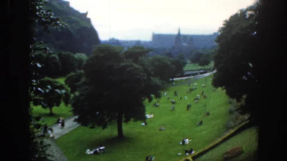 1961 Scotland 8mm view of people relaxing on a grassy Edinburgh park slope beneath the distant castle and city skyline.