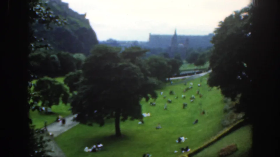 1961 Scotland 8mm view from above a public park, with scattered visitors on lawns, trees, paths, and distant buildings.