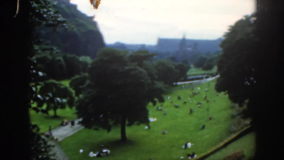 High-angle 1961 Scotland park scene with small groups on the lawn, mature trees, footpaths, and a soft distant skyline.