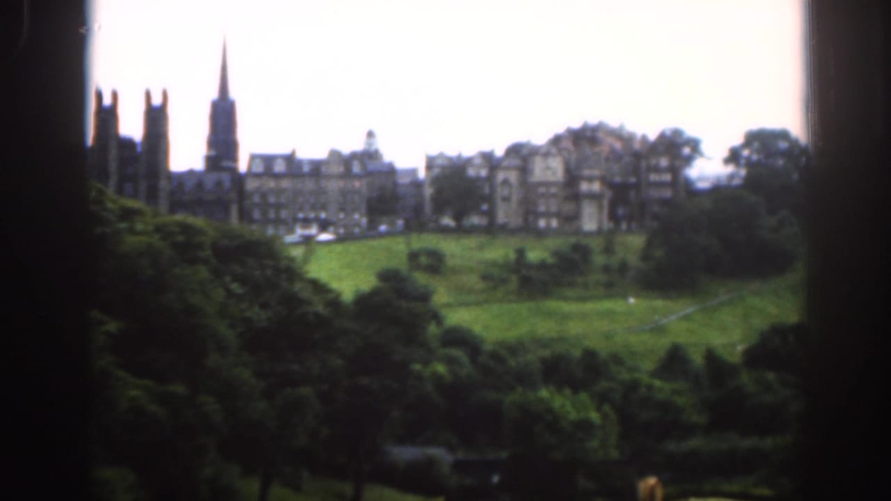 Green parkland and distant stone buildings seen through a dark window frame.
