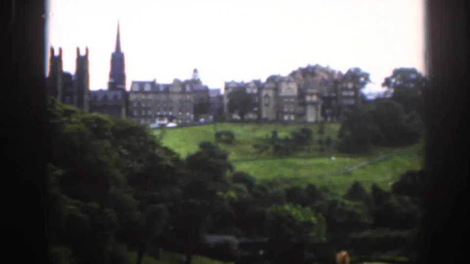1961 Scotland home-movie view of green parkland, trees and distant castle-like stone buildings framed by a dark window edge.