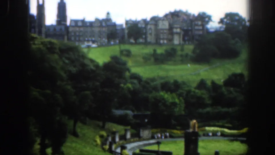 Elevated 1961 Scotland garden view with a curved path, hedges, lawn, distant visitors and stone buildings in the background.