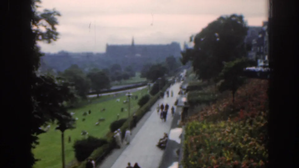 1961 Scotland home-movie view of a park path, lawn, flowerbeds, trees, and a distant castle-like landmark under an overcast sky.