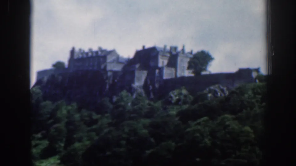 Final 1961 Scotland home-movie frame of a castle-like landmark above trees, softened by exposure and handheld 8mm texture.