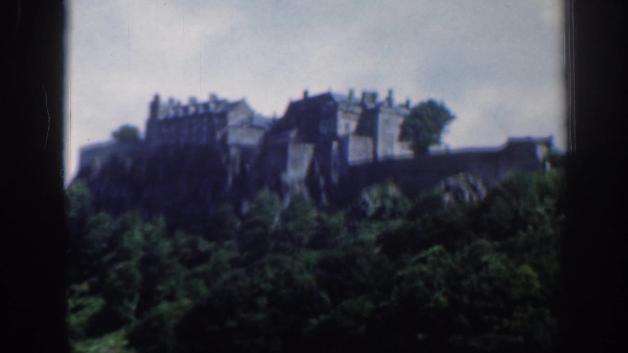 1961 Scotland 8mm frame showing Edinburgh Castle on a rocky rise beyond green trees and fields under a cloudy sky.