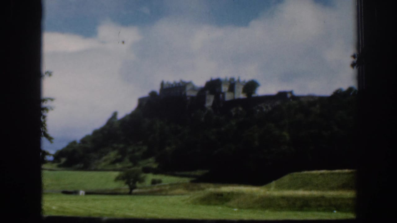 1961 Scotland home-movie frame with Edinburgh Castle seen across parkland, partially silhouetted against a bright cloudy sky.