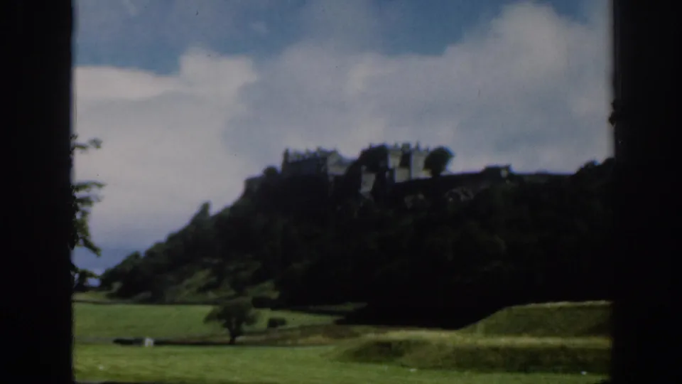 1961 Scotland 8mm frame showing Edinburgh Castle from a low parkland viewpoint with soft focus and dark frame edges.