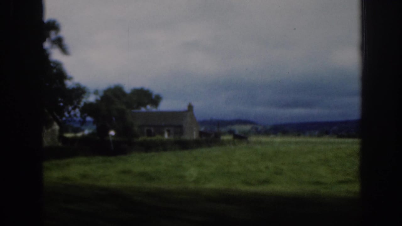 1961 Scotland home-movie view of an open green field, dark trees, and a distant stone building beneath overcast sky.