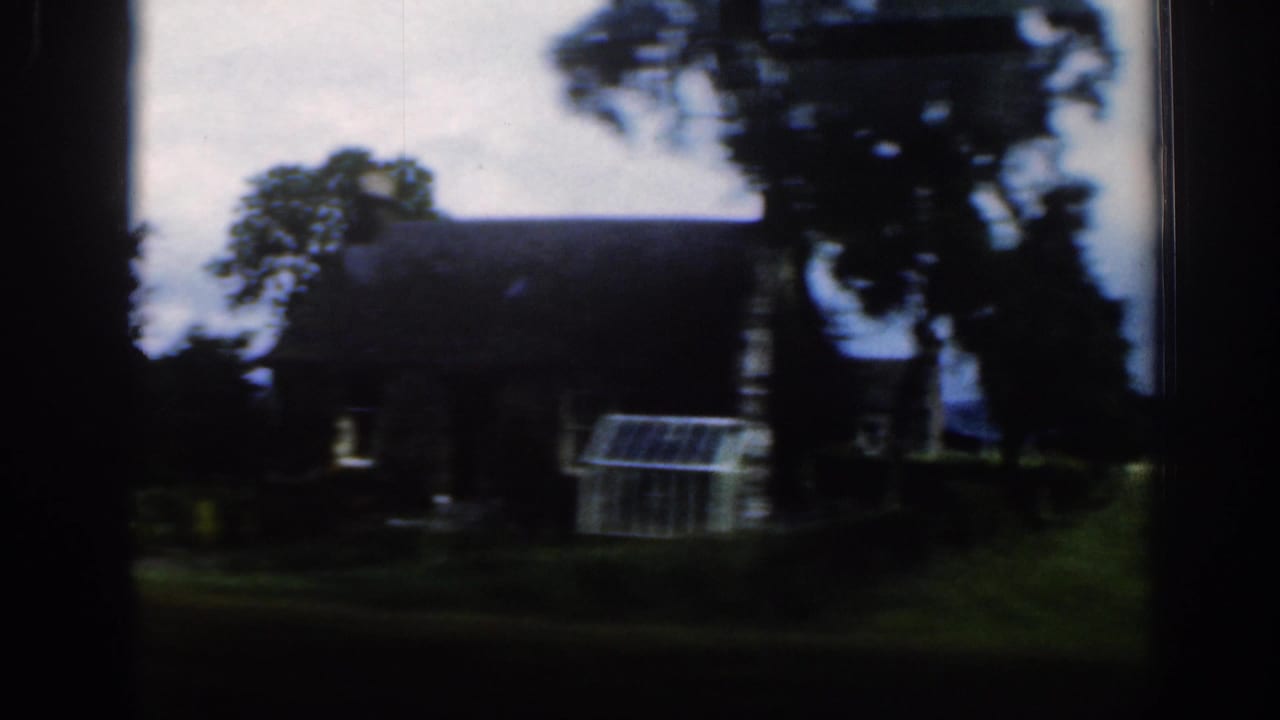 Dark stone building with trees and a small glasshouse-like structure nearby.