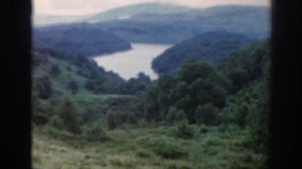 1961 Scotland landscape view of a winding loch between forested green hills and soft distant ridges under cloud.