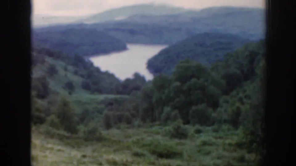 1961 Scotland 8mm view of a loch set between wooded green hills, partially blocked by dark window bars.
