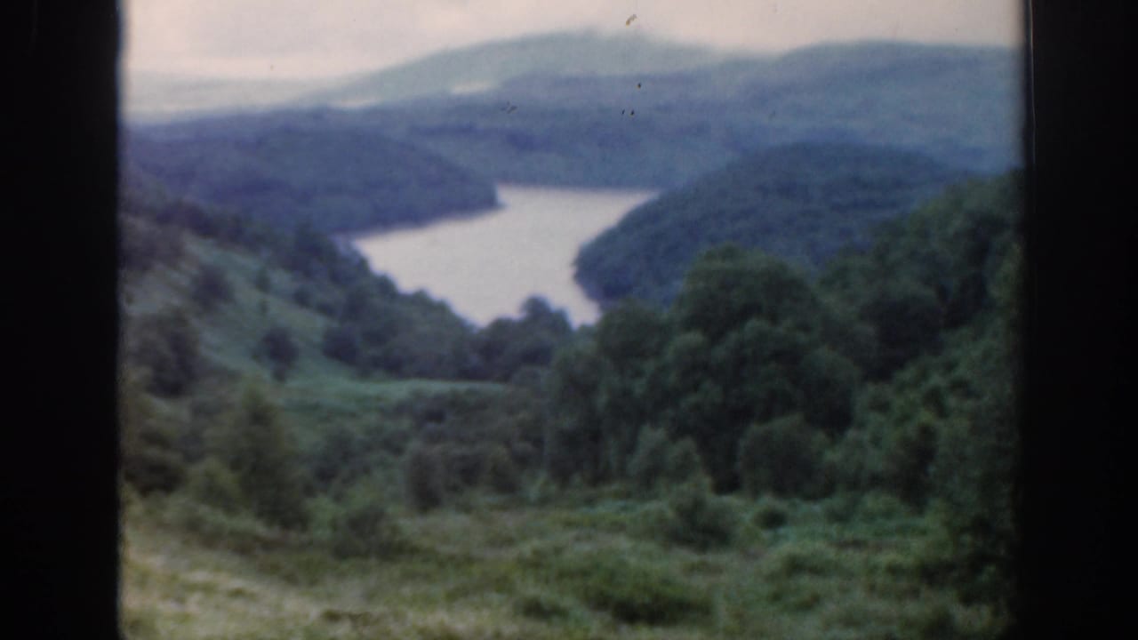 Similar loch and hillside view with dark vertical window bars in front.
