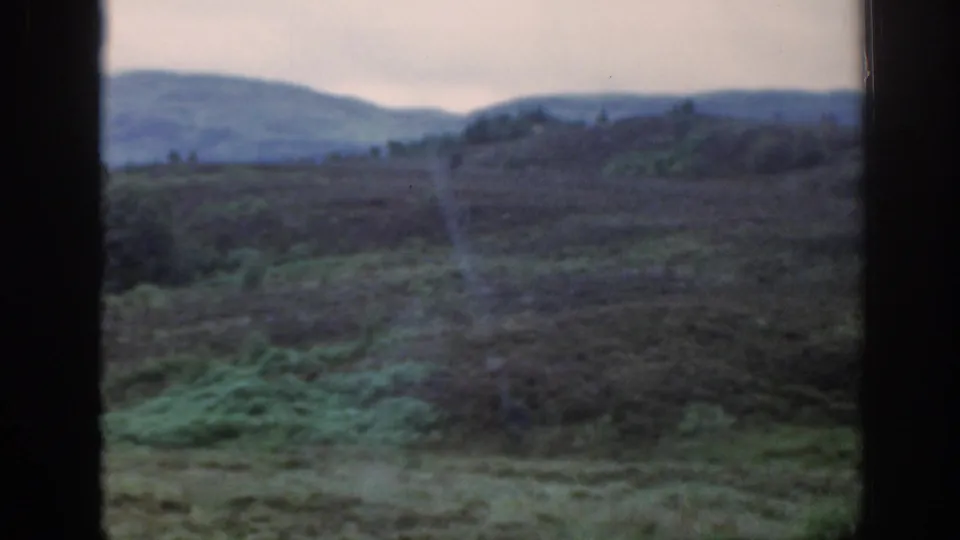 1961 Scotland 8mm frame of rough moorland with low rolling hills beyond, viewed through a dark window frame.