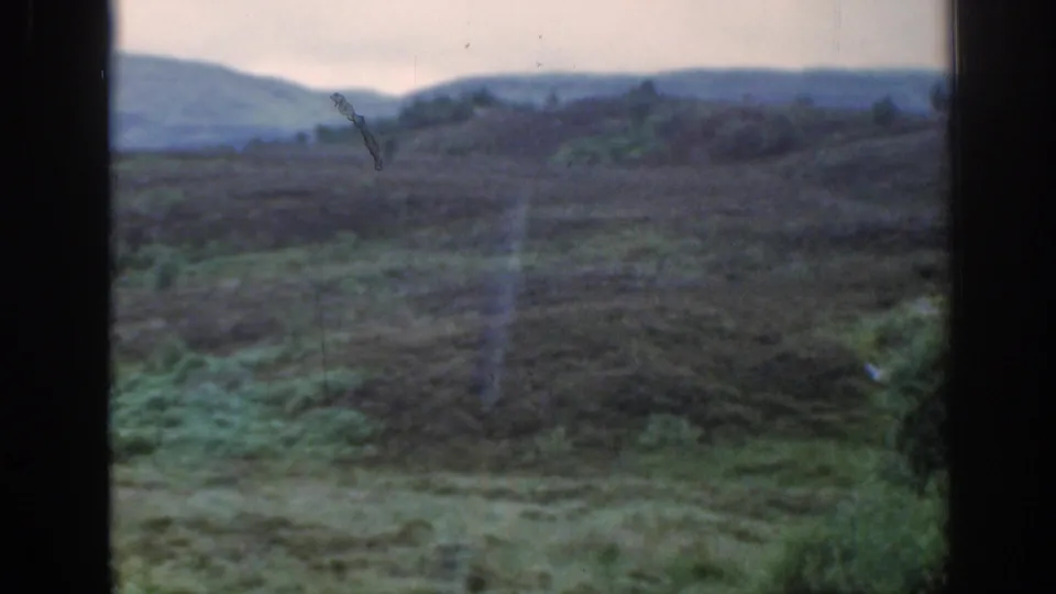 Soft 8mm view of Scottish moorland and rolling hills under an overcast sky, with window framing visible.