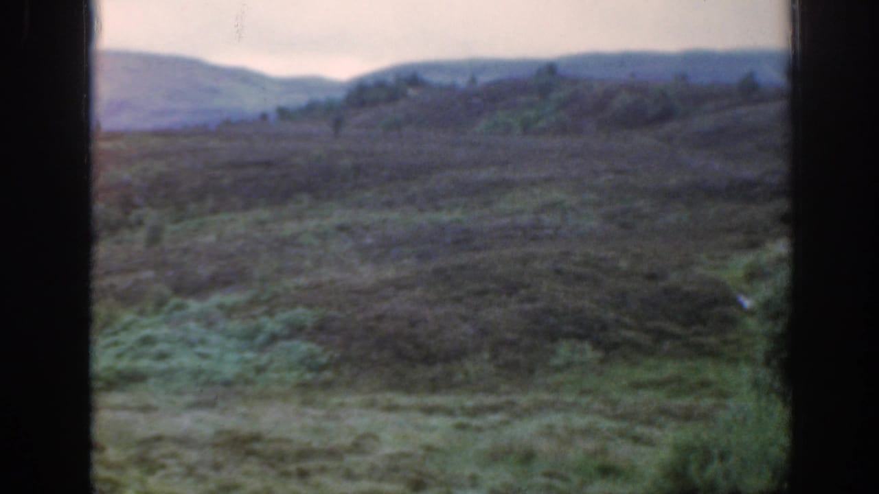 1961 Scotland 8mm frame of muted green and purple moorland with distant hills and dark vertical frame borders.