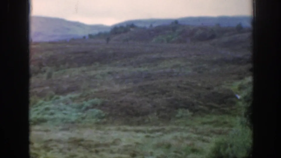 1961 Scotland 8mm frame of muted green and purple moorland with distant hills and dark vertical frame borders.