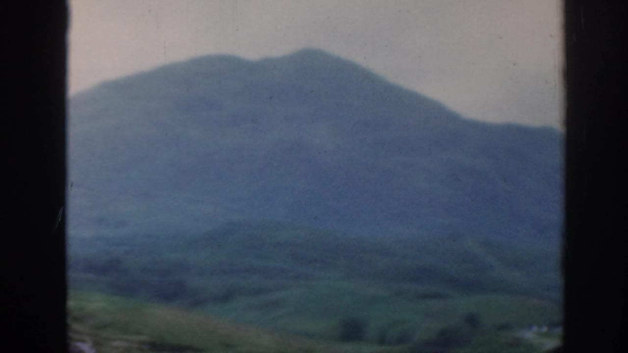Blue-green mountain landscape seen through dark car-window edges.