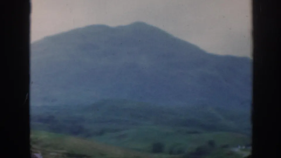 1961 Scotland home-movie view of hazy blue-green mountains framed by dark car-window edges.