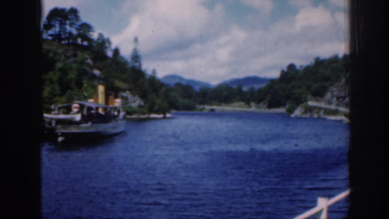 1961 Loch Katrine view from a moving vessel, with a small steamboat near wooded shore and distant hills.
