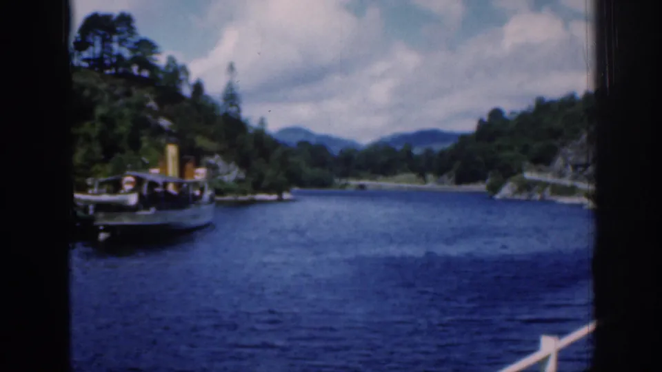 1961 Loch Katrine view from a moving vessel, with a small steamboat near wooded shore and distant hills.